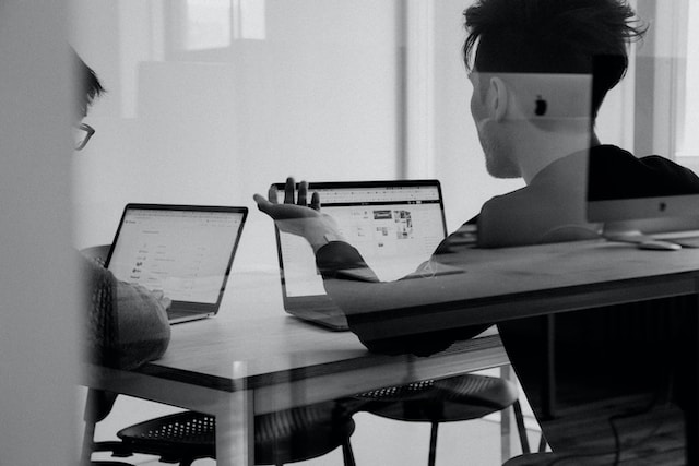 two people silhouettes at an office talking next to laptops
